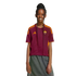 A young person with long braids smiles, wearing a maroon and orange AS Roma jersey and a grey skirt against a black background.