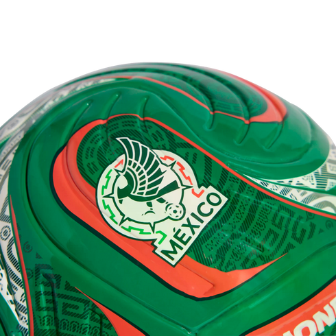 Close-up of a glossy green soccer ball featuring the Mexico national team crest, with red and white accents and textured patterns.