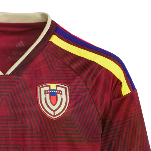 Close-up of a maroon Adidas Venezuela national soccer jersey with a geometric pattern, the team crest, and yellow and blue shoulder stripes.