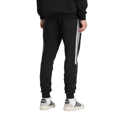 Back view of a person wearing black Adidas track pants with white side stripes and white sneakers.