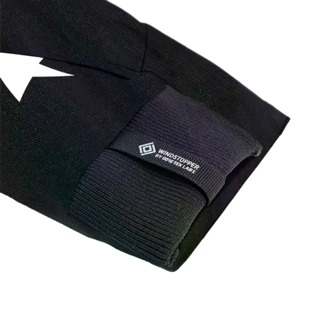 Close-up of a black sleeve featuring a ribbed cuff and a small tag with the text "WINDSTOPPER BY GORE-TEX LABS" and a diamond logo.
