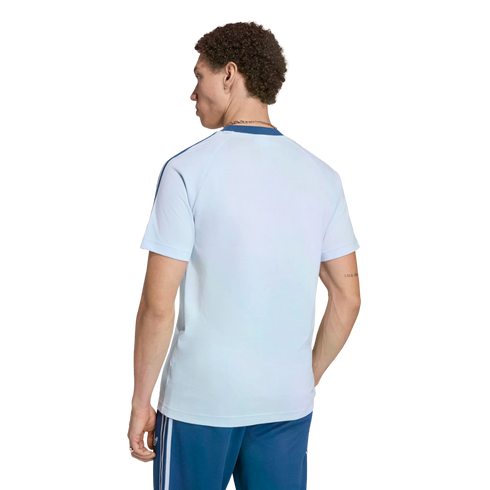 A man from behind, wearing a light-blue short-sleeved t-shirt with dark blue shoulder stripes and dark blue shorts with white side stripes, against a black background.