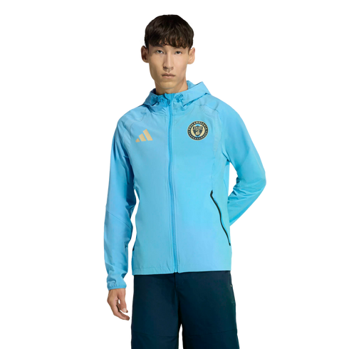 Male model in a light blue Philadelphia Union zip-up hoodie and dark blue shorts, set against a black background.