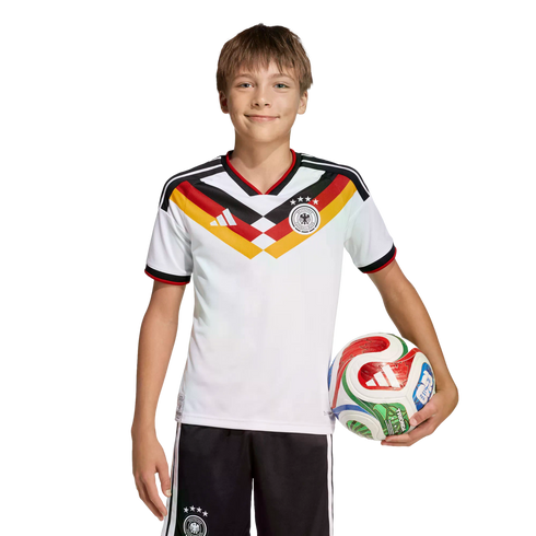 A smiling boy in a German national soccer uniform holds a colorful soccer ball against a black background.