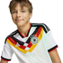 A smiling young boy with light brown hair wearing a white German national football team jersey featuring a black, red, and yellow graphic design.