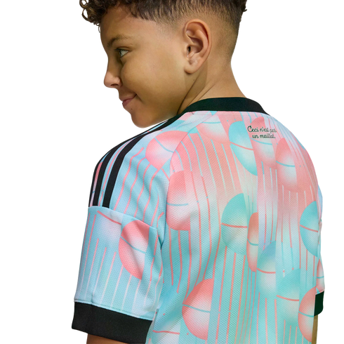 Side view of a boy in a pink and light blue patterned sports jersey with black stripes. Text on the back reads "Ceci n'est pas un maillot." Set against a black background.