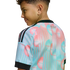 Side view of a boy in a pink and light blue patterned sports jersey with black stripes. Text on the back reads "Ceci n'est pas un maillot." Set against a black background.