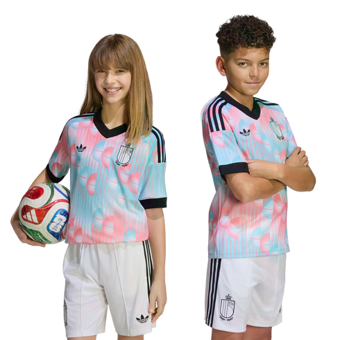 A boy and girl in matching pink and blue patterned soccer jerseys and white shorts pose against a black background. The girl holds a soccer ball.