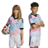 A boy and girl in matching pink and blue patterned soccer jerseys and white shorts pose against a black background. The girl holds a soccer ball.