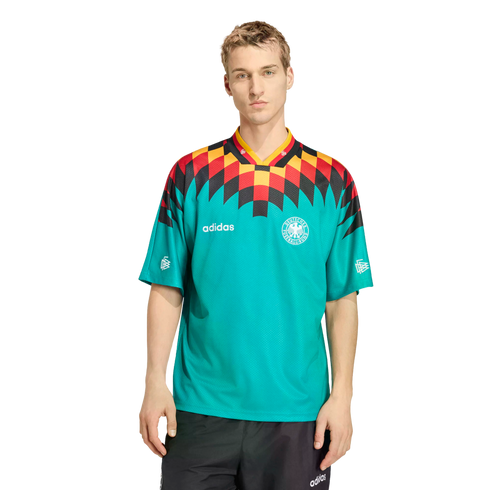 A man models a teal Adidas Germany soccer jersey with a bold black, red, and yellow geometric shoulder pattern, paired with black athletic shorts against a white background.