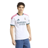 A young man with curly hair modeling a white Real Madrid home jersey and blue jeans against a white background.