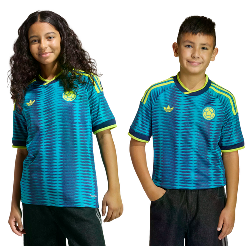 Two children smile while wearing matching teal and blue patterned Colombia national team soccer jerseys with yellow accents.
