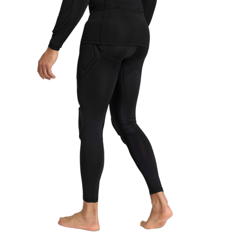 Rear view of a person wearing black padded compression leggings and a long-sleeved athletic top, standing barefoot against a plain light gray background.