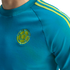 Turquoise shirt with three neon green shoulder stripes and an embroidered Colombian Football Federation logo on the chest.