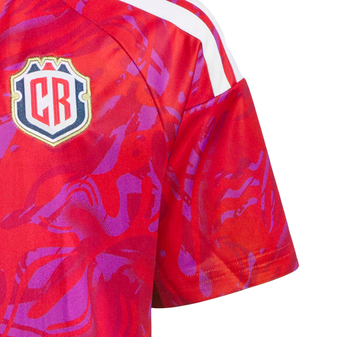Close-up of a red sports jersey with a purple abstract pattern, white shoulder stripes, and a shield-shaped crest featuring the letters "CR".