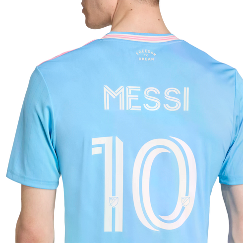 Back of a light blue soccer jersey with "MESSI" and "10" in white. It features pink trim and the words "FREEDOM TO DREAM" printed on the upper back.