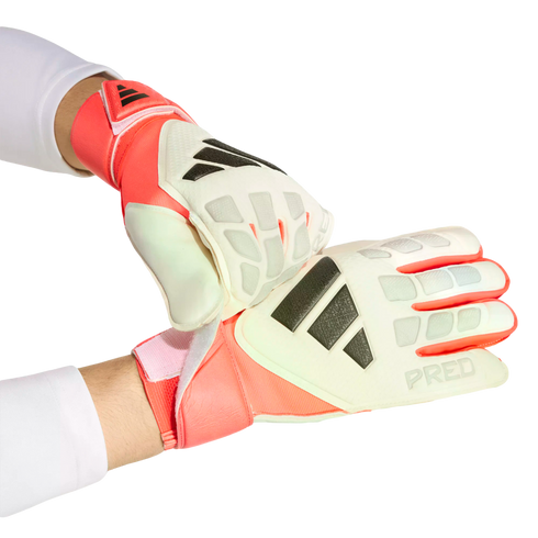 Person wearing white and coral Adidas Predator goalkeeper gloves, adjusting a wrist strap against a black background.