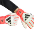 A person wears red, white, and black Adidas Predator goalkeeper gloves against a solid black background. One hand is clenched in a fist, and the other is open.