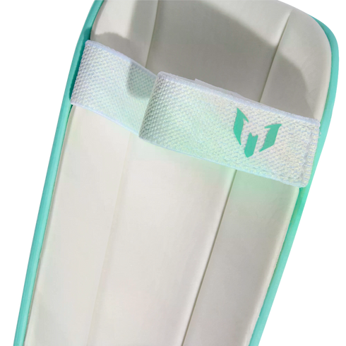 Close-up of a white and teal soccer shin guard featuring an iridescent elastic strap with a teal Messi logo.