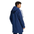Rear three-quarter view of a man wearing a long navy blue hooded parka featuring three white stripes on the sleeves.