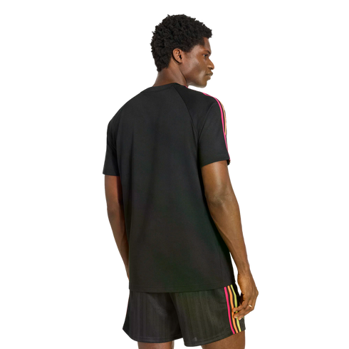 Rear view of a man looking over his shoulder, wearing a black t-shirt and matching shorts with pink, orange, and yellow stripes on the sides. He is set against a black background.