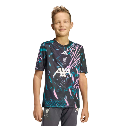 A young boy smiling in a dark Liverpool FC training jersey with pink and teal patterns and grey shorts against a black background.
