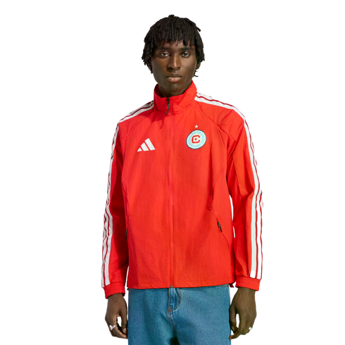 Man wearing a red Adidas track jacket with a Chicago Fire FC crest and blue jeans, standing against a black background.