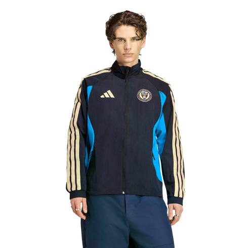 A man in a navy blue Adidas Philadelphia Union track jacket with cream stripes and blue side panels, posed against a black background.