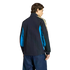 Rear view of a person in a black track jacket with blue side panels and cream stripes, wearing navy blue pants, against a black background.