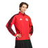 A young man wearing a red New York Red Bulls Adidas track jacket with black stripes, posing with hands on hips against a black background.