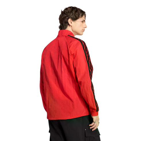 Rear-side view of a man in a red jacket with black patterned stripes on the sleeves and dark cargo pants against a black background.