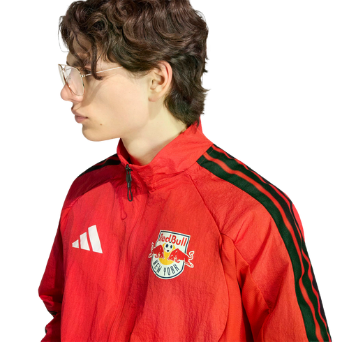 Side profile of a young person with glasses wearing a red Adidas New York Red Bulls track jacket against a black background.