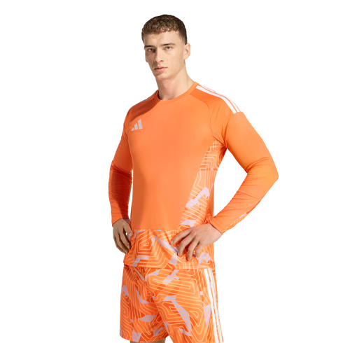 A man wearing a bright orange Adidas goalkeeper kit with geometric patterns on the jersey and shorts, posing against a solid black background.