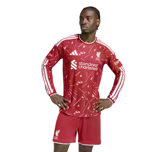 A man wearing a red and white patterned long-sleeved Liverpool F.C. jersey and matching shorts stands with his hands on his hips against a white background.