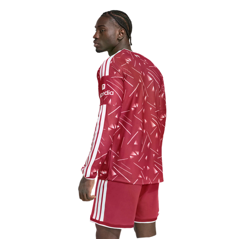 A man with braided hair in a red patterned long-sleeved soccer kit with white stripes, looking away against a white background.