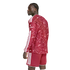 A man with braided hair in a red patterned long-sleeved soccer kit with white stripes, looking away against a white background.