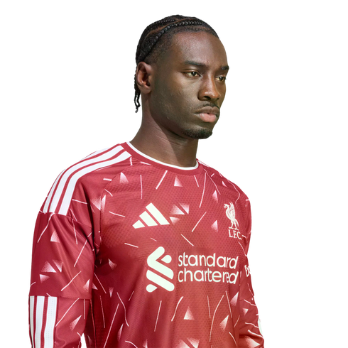 A man with braided hair wearing a patterned red Liverpool FC jersey against a white background.