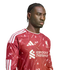 A man with braided hair wearing a patterned red Liverpool FC jersey against a white background.