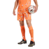 A person from the waist down wearing an orange patterned soccer kit and black cleats, holding a soccer ball against a solid black background.
