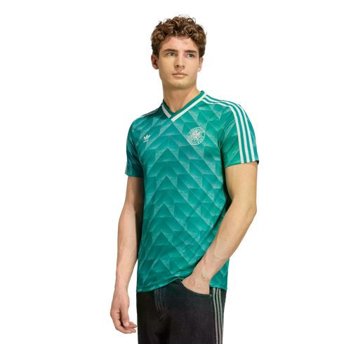 A young man wearing a green Adidas Germany soccer jersey with a white geometric pattern, standing against a white background.