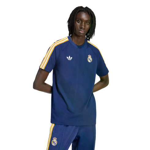 A man wearing a navy blue Adidas Real Madrid t-shirt and matching track pants with yellow and white stripes against a solid black background.