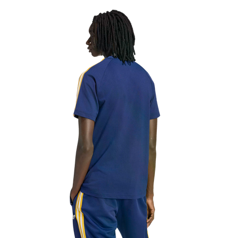 Back view of a person with dreadlocks in a navy blue t-shirt and matching pants with yellow and white stripes, standing against a black background.