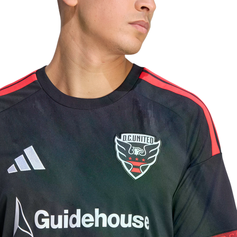Close-up of a person wearing a black D.C. United soccer jersey with red shoulder stripes, featuring the team crest, white Adidas logo, and Guidehouse sponsor logo.