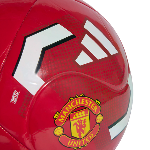 Close-up of a glossy red soccer ball featuring the Manchester United club crest and white Adidas stripes against a textured red background.