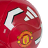 Close-up of a glossy red soccer ball featuring the Manchester United club crest and white Adidas stripes against a textured red background.