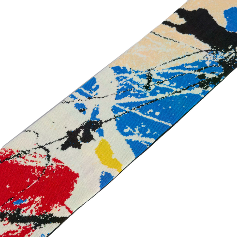 A diagonal strip of knit fabric featuring an abstract paint-splatter pattern in red, blue, yellow, and black on an off-white base.