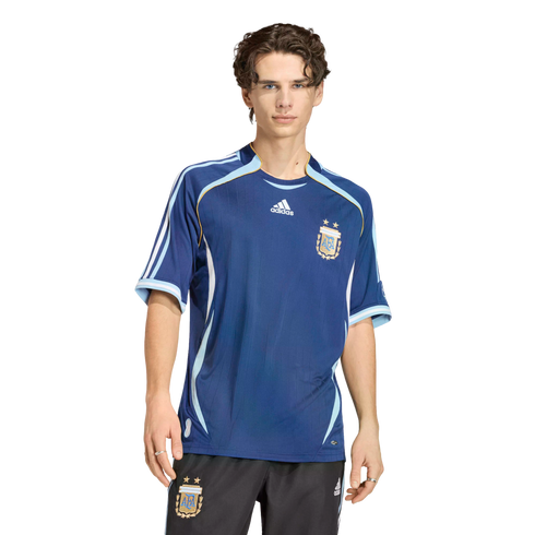 A man wearing a dark blue Adidas Argentina national team soccer jersey and black shorts against a solid black background.