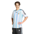 A man in a striped Argentina national football jersey and black shorts poses with his hands on his hips against a black background.