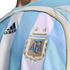 Close-up of an Argentina football jersey with light blue and white stripes, featuring an embroidered AFA crest with two gold stars and the Adidas logo.