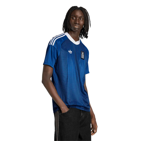 A man models a blue Adidas Greece national team jersey with white shoulder stripes and a white V-neck collar against a solid black background.